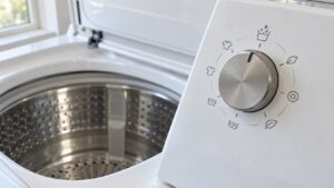 A close view of the cycle selector dial on a white top-load washing machine with the pointer set to the Clean Washer position and the empty drum visible behind it